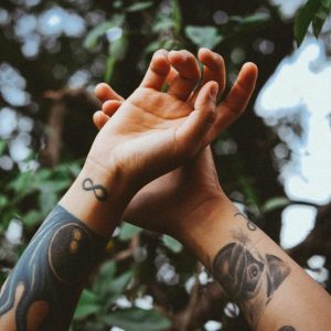 Close-up of tattooed hands reaching out against a blurry natural backdrop.