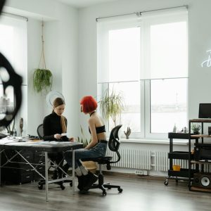 A modern tattoo studio with two women discussing plans. Neon art and bright interior lighting set the scene.