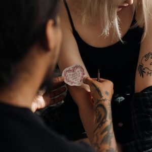 A tattoo artist creating a tattoo on a woman's arm, showcasing detailed design work.
