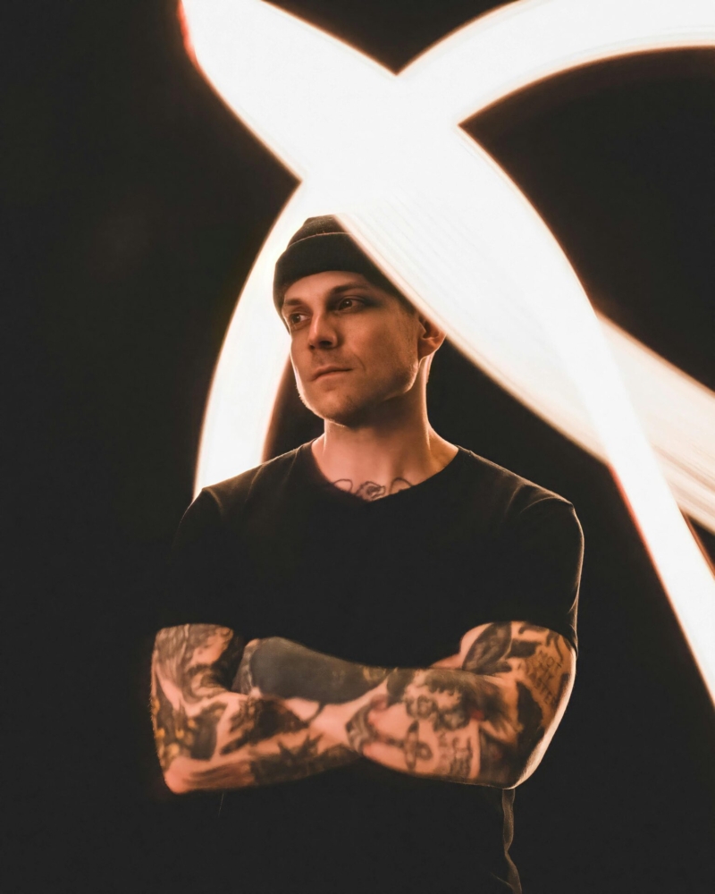 Portrait of a tattooed man in a black shirt posing under dynamic light trails.