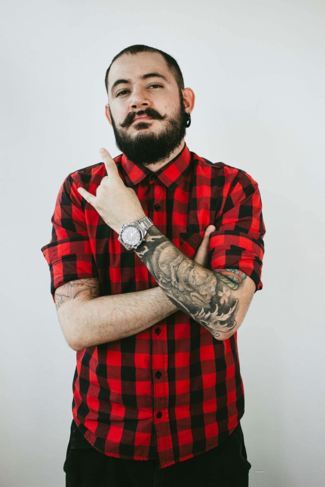 Confident tattooed man posing with crossed arms in a studio setting.